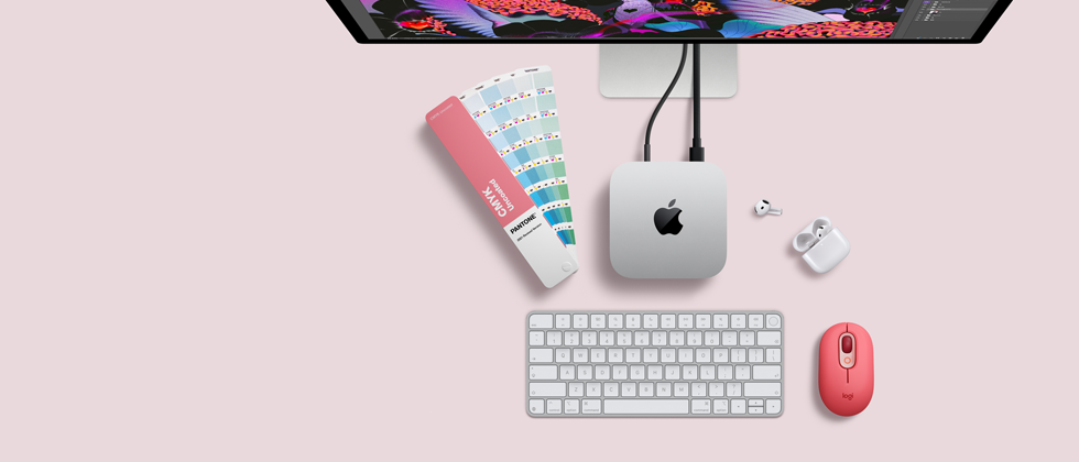 Mac mini, отгоре, сребърен алуминий, заоблени ъгли, гланцирано черно лого на Apple в центъра, свързано с кабел, Studio Display е частично видим отгоре, AirPod 4, отворени, Pantone цветови мостри и цифрова клавиатура, и мишка