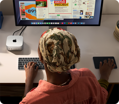 Άτομο που πληκτρολογεί σε γραφείο με Mac mini, συνδεδεμένη οθόνη Studio Display, Magic Keyboard, Magic Trackpad, διάφορα αντικείμενα