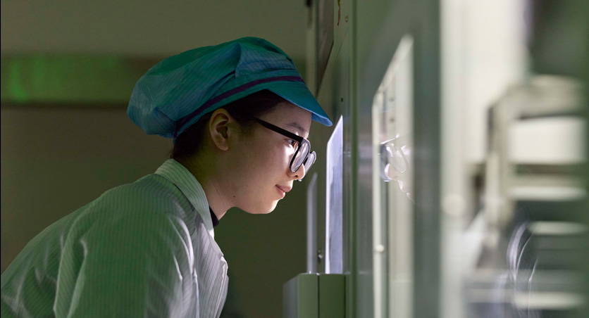 An employee in full-coverage work suit and eye wear observes Apple Watch assembly