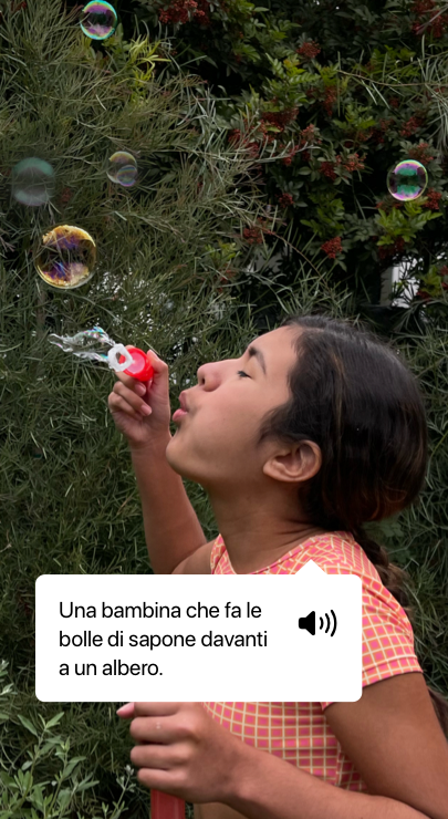 VoiceOver che descrive una foto e mostra il testo pronunciato: ‘Una bambina che fa le bolle di sapone davanti a un albero.’