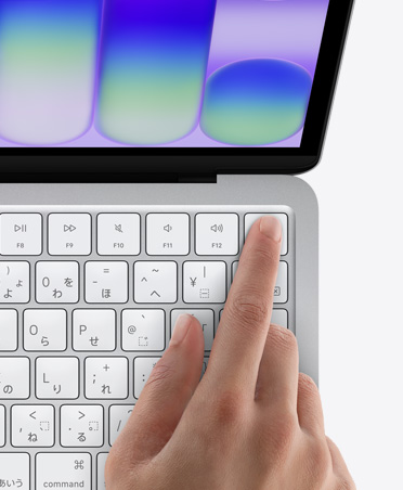 シルバーのMacBook Neo。キーボードの右上角にあるTouch IDセンサーに人の指が触れている
