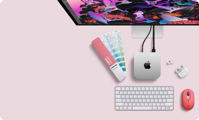 „Mac mini“ iš viršaus: sidabro spalvos aliuminio korpusas, užapvalinti kampai, centre – blizgus juodas „Apple“ logotipas, prie įrenginio prijungtas laidas; viršuje iš dalies matomas „Studio Display“, atidarytas „AirPods 4“ dėklas, „Pantone“ spalvų pavyzdžiai, skaičių klaviatūra ir pelė.