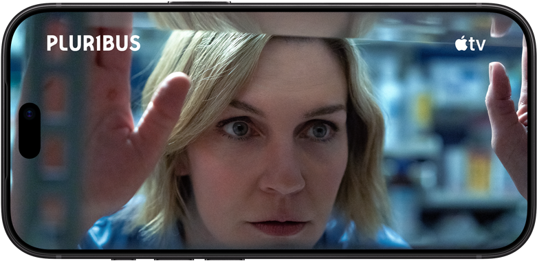 iPhone 18 Pro, horizontāli, tuvplānā redzama sieviete, kas skatās cauri plauktam. Seriāla nosaukums: Pluribus