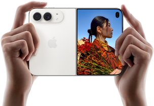 iPhone&nbsp;Duo, zvaigžņu baltā krāsā, tiek turēts rokās horizontālā novietojumā, atvērts, kreisajā panelī redzamas 48&nbsp;MP Dual&nbsp;Fusion aizmugurējās kameras, labajā panelī redzams, kā ārējā displejā tiek uzņemta cilvēka bilde, fotografējamais redz savu seju, kamēr tiek uzņemta bilde ar Duo&nbsp;Preview