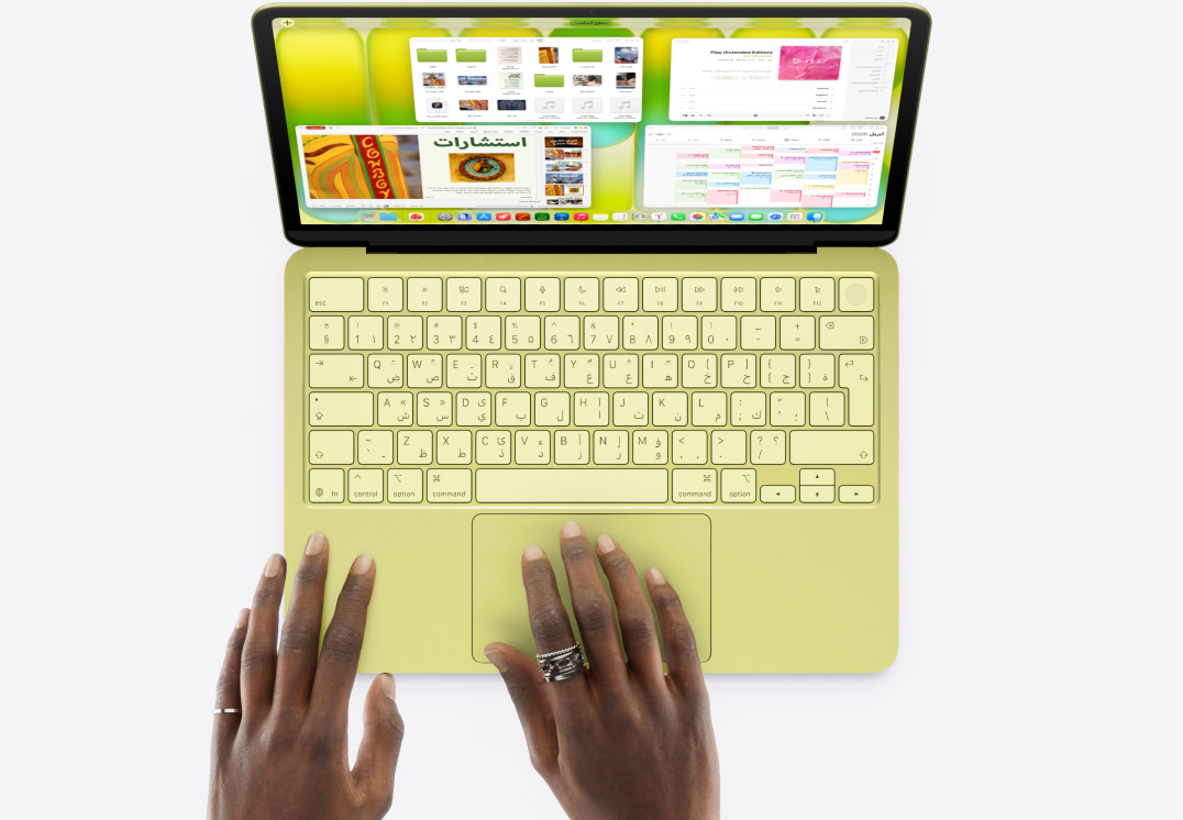 جهاز MacBook Neo، أصفر سيتروس، يد شخص على لوحة التعقب، نوافذ متعددة مفتوحة تشمل تطبيقات الموسيقى والتقويم وMicrosoft PowerPoint
