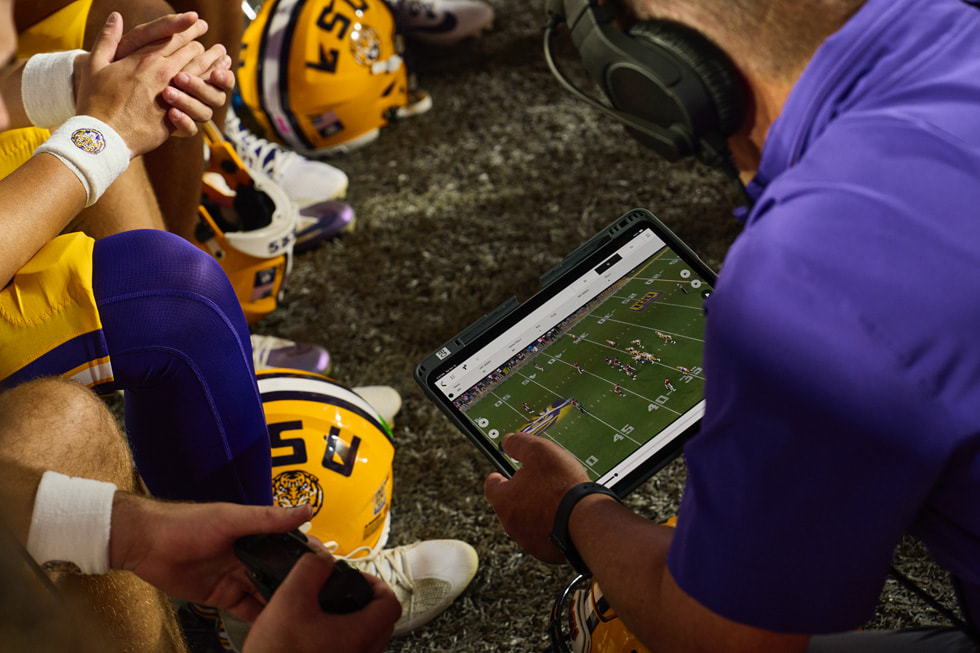 Das Trainerteam und die Spieler:innen der LSU überprüfen während eines Footballspiels an der Seitenlinie Aufnahmen auf dem iPad Pro.

