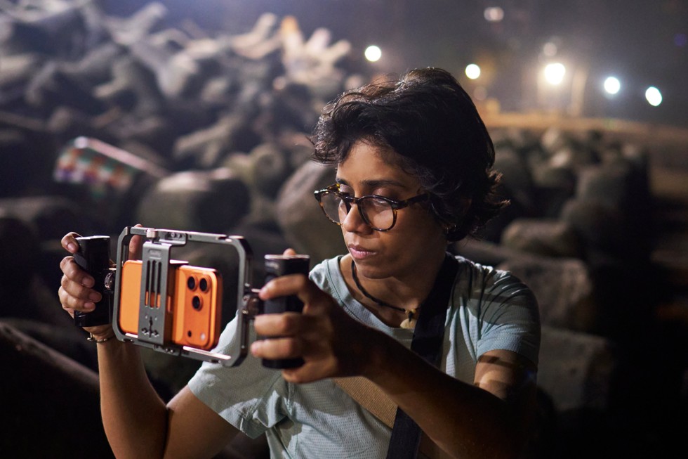 Shreela Agarwal segura um rig de câmera com um iPhone 17 Pro Max acoplado, filmando ao ar livre à noite.