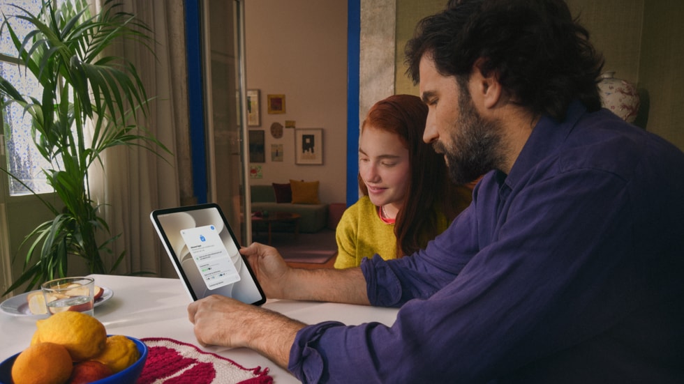 شخص وطفل يجلسان معاً على طاولة خشبية، ويتفاعلان مع جهاز iPad.
