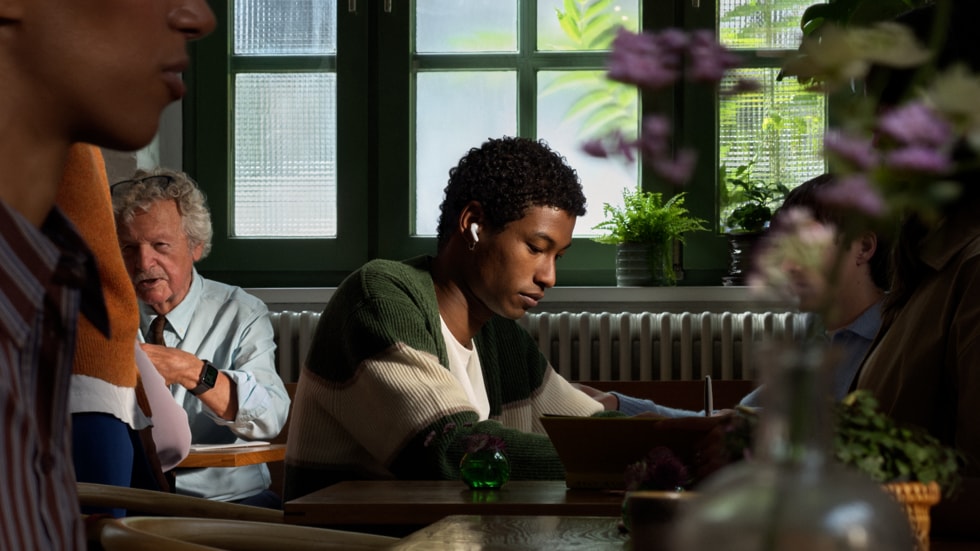 Eine Person mit AirPods 5 bei der Arbeit in einem Restaurant inmitten anderer Personen.