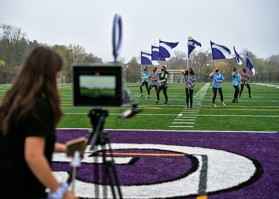 Eine Schülerin der New Rochelle High School verwendet ein iPad, um Mitschüler:innen mit Flaggen auf dem Sportplatz aufzunehmen.

