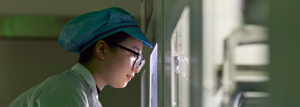 An employee in full-coverage work suit and eye wear observes Apple Watch assembly