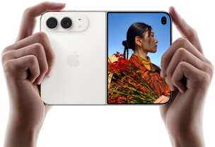 iPhone Duo v nebeskej bielej farbe, držia ho dve ruky v orientácii na šírku, je rozložený, na ľavom paneli vidno 48 Mpx zadné kamery Dual Fusion, na pravom paneli vidno na vonkajšom displeji fotografovanú osobu, ktorá vďaka funkcii Duo Preview vidí pri fotení svoju tvár