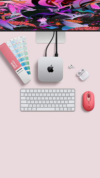 Pohľad zhora na strieborný hliníkový Mac mini so zaoblenými rohmi a lesklým čiernym logom Apple uprostred. Káblom je pripojený k displeju Studio Display, ktorý je čiastočne vidieť navrchu. Vedľa sú otvorené slúchadlá AirPods 4, vzorky farieb Pantone, numerická klávesnica a myš.