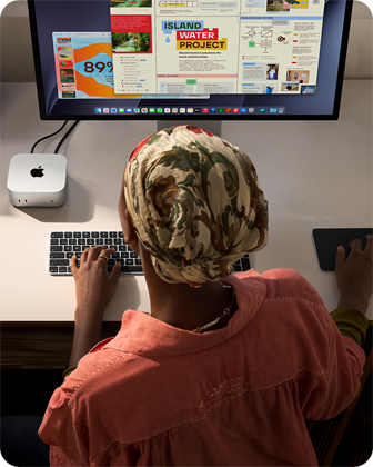 Людина за робочим столом друкує на Mac mini, до якого підʼєднано Studio Display, клавіатура Magic Keyboard, трекпед Magic Trackpad, різноманітні предмети