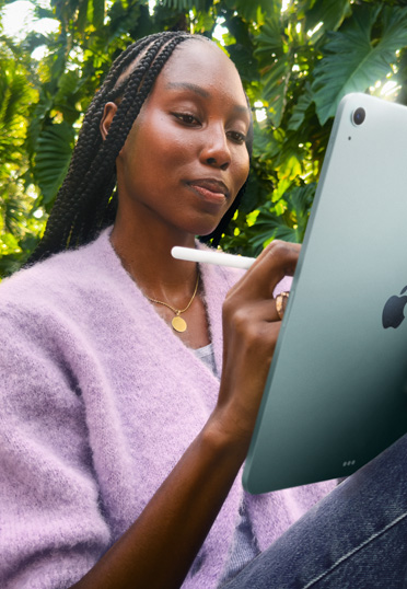 A student sitting outdoors. She's holding an iPad and an Apple Pencil Pro.
