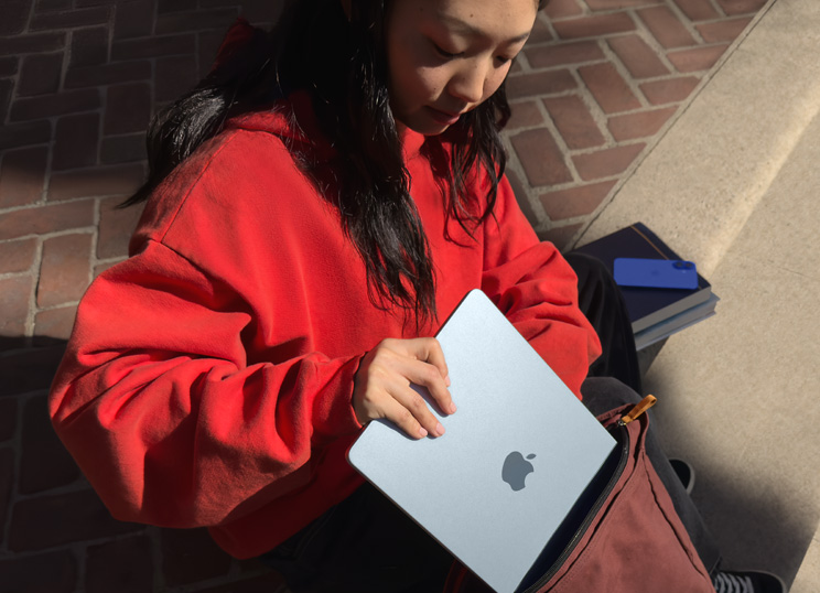 Uma pessoa sentada em degraus de pedra a guardar o MacBook na mochila.