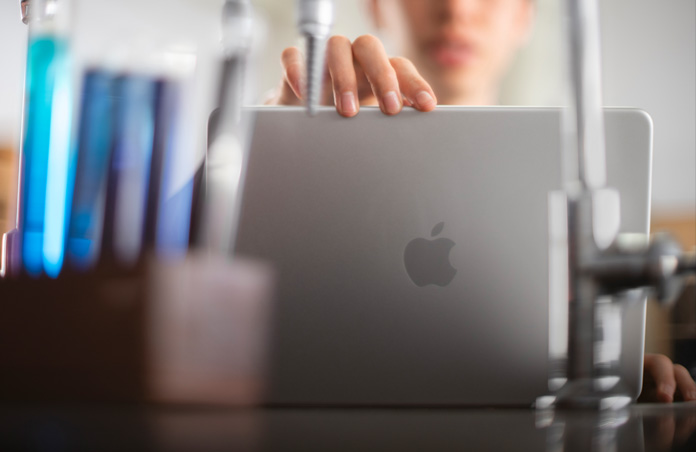 Un estudiante apoya sus dedos en el delgado marco de un MacBook abierto en un laboratorio