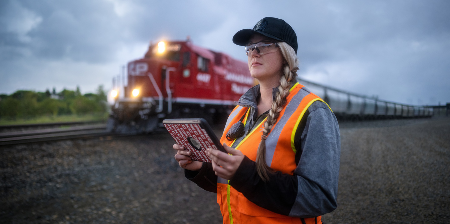 A railroad worker holds an iPad and looks out at the tracks as a train passes by