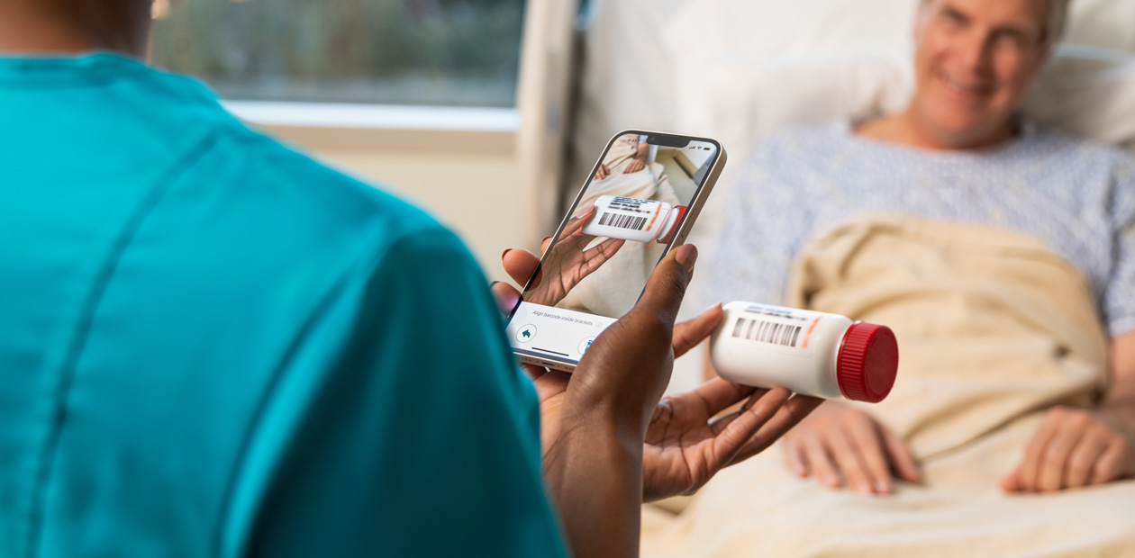 A nurse in teal scrubs scans a patient’s medicine with her iPhone.