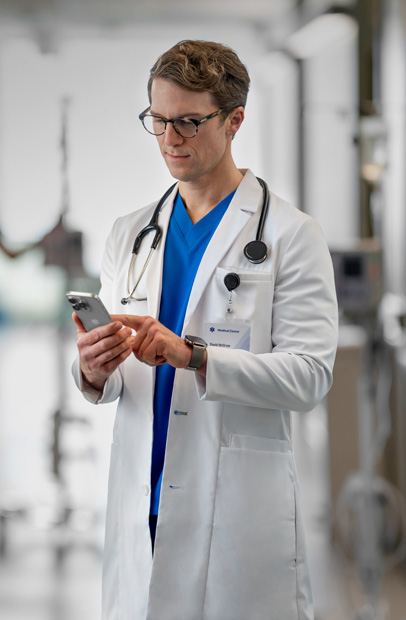 A male provider looking at his iPhone reviewing patient progress in a hospital.