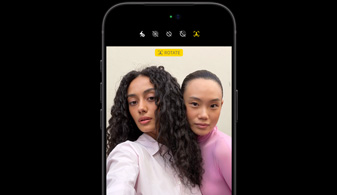Melna iPhone 18 Pro priekšpuses skats, kurā ir redzamas divas personas ar sejas izsekošanas funkciju, demonstrē Center Stage priekšējās kameras funkciju