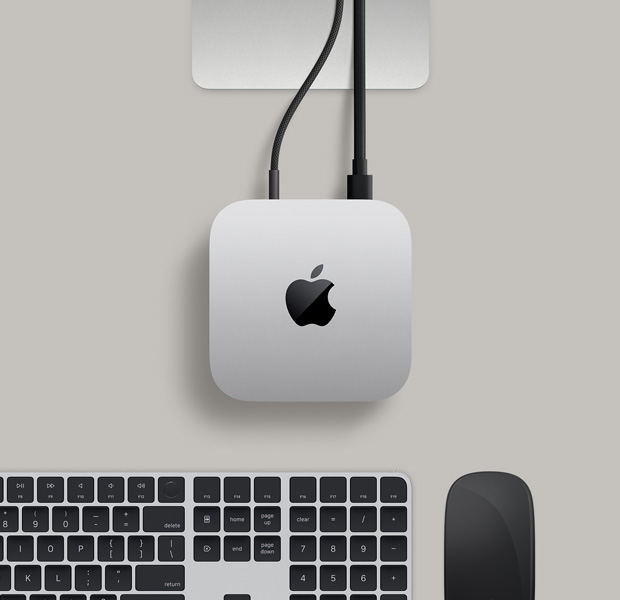 Top view of silver Mac mini, with two cords plugged from the back ports into a display monitor, next to a black Magic Mouse and black Magic Keyboard