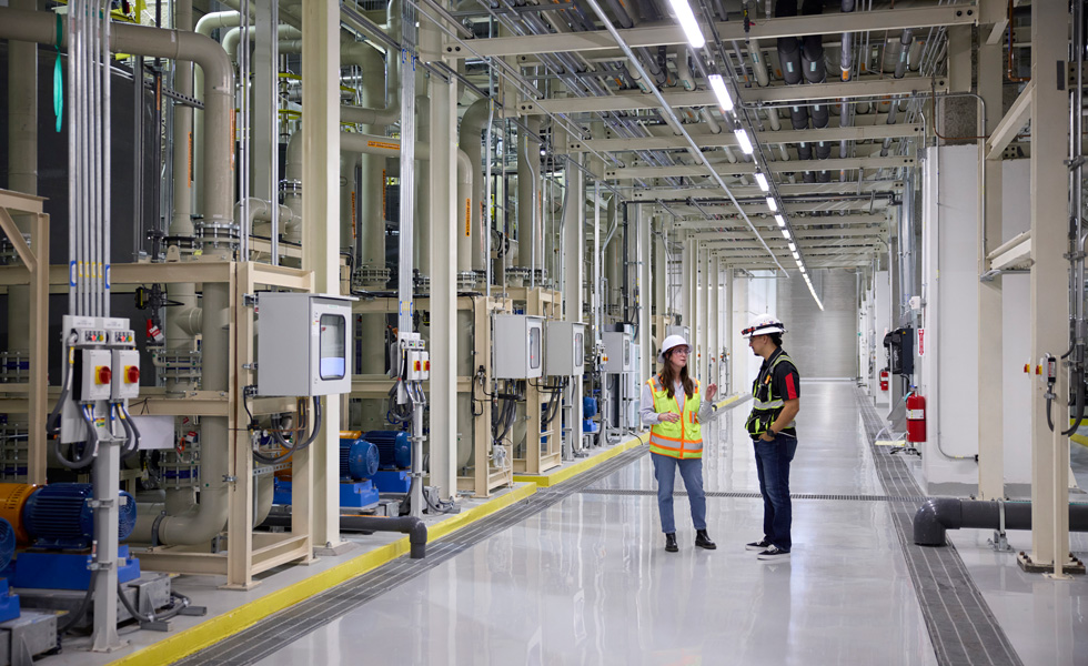 Two employees wearing safety clothing talk in the hallway of a manufacturing facility